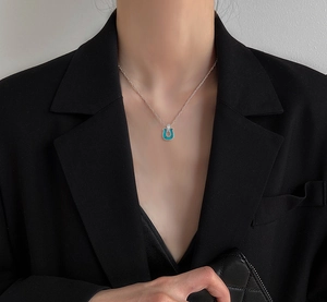 Close-up of horseshoe pendant necklace with turquoise stone inlay on model in black suit
