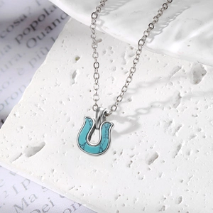 Minimalist horseshoe turquoise pendant necklace with a polished steel chain on stone base