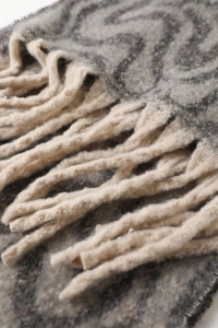 Macro shot of grey geometric wave knit scarf with thick cream tassel detail and warm texture