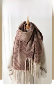 Détail d'une écharpe d'hiver aux motifs géométriques marron et franges sur un manteau blanc