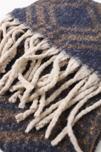 Gros plan sur la maille géométrique bleu marine et marron et les glands d'une écharpe