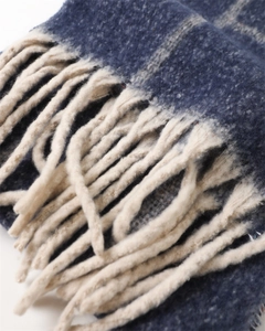 Detailed close-up of dark blue plaid scarf showing soft cashmere-like texture and cream tassels