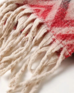 Macro detail of red zigzag patterns and thick beige yarn tassels on a warm winter shawl