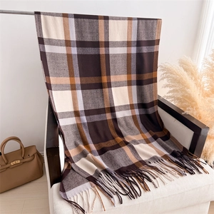 Detail of plaid cashmere-feel scarf with long tassels draped on a white armchair