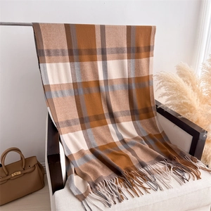 Detail shot of a warm plaid cashmere-feel scarf with long tassels on a white chair