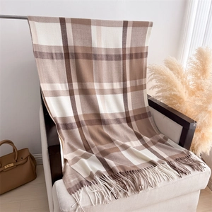 Detail of checkered cashmere shawl with fringes draped on a white chair in a warm setting