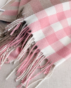 Detail of soft plaid scarf featuring pink, white, and brown knit textures with fringe