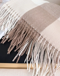 Détail du tissage en chevrons et longues franges sur une écharpe d'hiver à carreaux