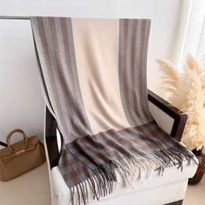 Detail of plaid color-block knit shawl with fringe on an armchair in warm setting