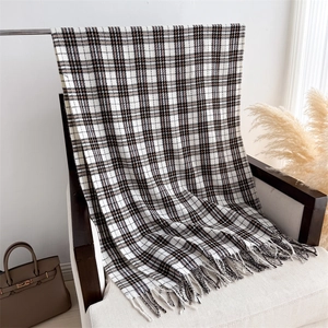 Detail of plaid cashmere-like scarf featuring tassels draped on an armchair
