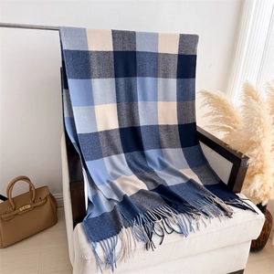 Détail d'une écharpe à carreaux bleu marine et beige avec franges sur un canapé