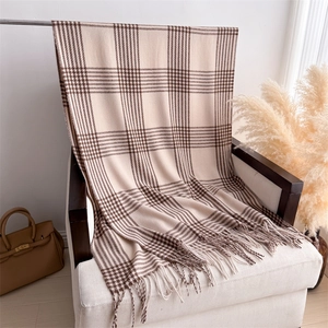 Detail of plaid cashmere scarf with soft fringes hanging on white fabric chair