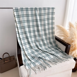 Close-up of grey-green plaid scarf with soft fringe on a cozy white armchair
