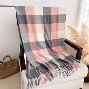 Détail d'une écharpe à carreaux rose et gris avec de longues franges sur une chaise