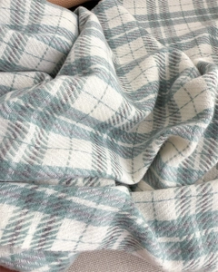 Detail of soft cashmere-like knit fabric with a green and white plaid pattern and fringes