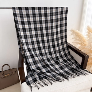 Detailed view of grey checkered cashmere scarf with elegant fringe on a white chair
