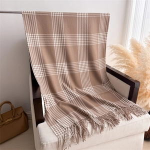 Detail of soft brown plaid scarf with long tassels draped on a white armchair