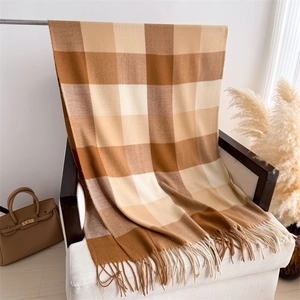 Gros plan d'une écharpe à carreaux douce avec franges marron et beige sur sofa