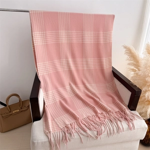 Detail of soft pink plaid cashmere scarf with hand-twisted fringe on white armchair