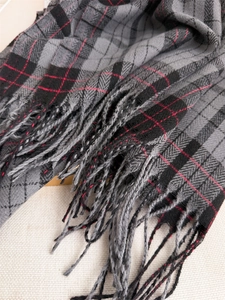 Close-up of classic grey and black plaid scarf texture with red stripes and soft fringe details