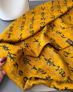 Close-up of yellow silk scarf with black Chinese calligraphy and jacquard patterns