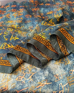 Macro detail of silk scarf showing vintage hieroglyphic patterns and Greek key border