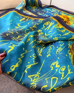 Macro shot of silk scarf showing glossy blue fabric with yellow calligraphy art pattern
