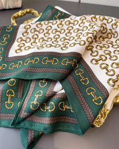 Detail of silk-like square scarf with horsebit chain print and green border on gold tray