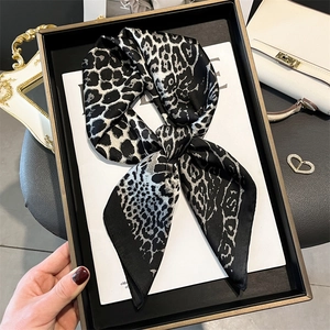 Elegant leopard print silk scarf styled in a bow on a black display tray with accessories