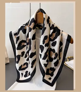 Detail of leopard print silk-like scarf with black border hanging on a wooden hanger
