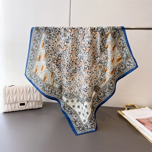 Detail of premium square silk scarf with blue paisley pattern and floral print texture