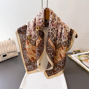 Elegant paisley floral printed silk scarf in earth tones hanging on a wooden hanger