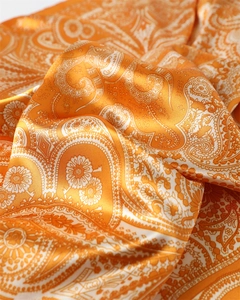 Gros plan détaillé du motif paisley orange sur le tissu satiné lisse du foulard