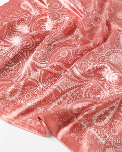 Détail d'un foulard en satin rose corail avec motif paisley et finitions cousues