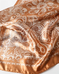 Détail du foulard en satin de soie avec motif paisley et finition ambrée élégante