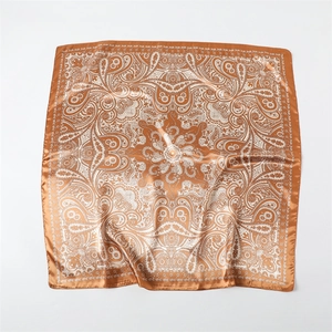 Détail d'un foulard carré en satin avec motif cachemire bronze et texture soyeuse lisse