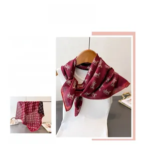 Detail of burgundy silk scarf showing golden vintage carriage pattern and satin texture