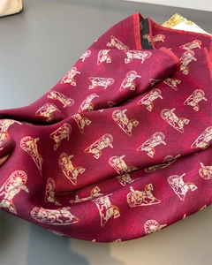 Detail of burgundy silk scarf showing classic gold carriage pattern and twill texture