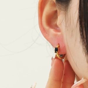 Close-up of a gold huggie hoop earring with marquise-cut black zircon on a model