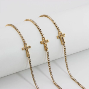 Trois bracelets de tennis en acier doré avec pendentifs croix en cristal sur socle blanc