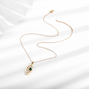 Detail of gold oval hollow pendant featuring a green heart-shaped zircon on a fine chain