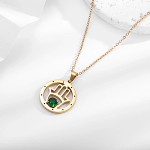 Titanium steel Hamsa necklace with gold plating and green gemstone on a white pedestal
