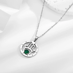 Close-up of silver Hamsa Hand pendant with emerald green stone on steel chain