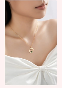 Detail of gold Hamsa Hand necklace with emerald green stone on a model in white satin
