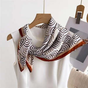 Detail eines Seidenschals mit braunem Spiralmuster und rotem Saum auf weißem Kleid