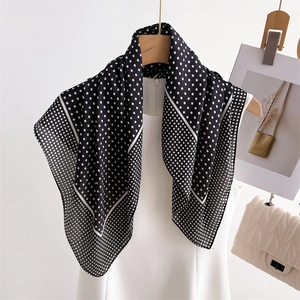 Elegant black and white polka dot silk-feel scarf draped on a minimalist white dress