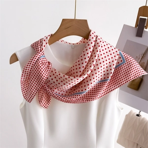 Close-up of elegant white silk scarf with red polka dots tied on a white blouse