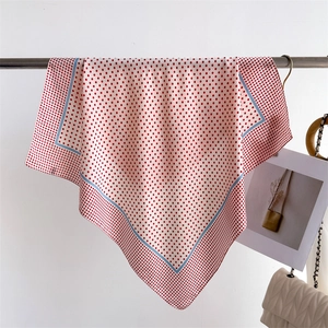 Detail of silk-like square scarf with red polka dots and light blue trim on white fabric