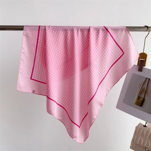 Pink silk-like scarf with white polka dots hanging on a metal rod for detail