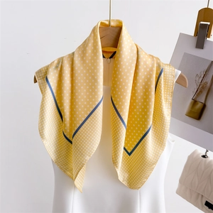 Elegant yellow polka dot silk scarf with blue border hanging on a wooden hanger
